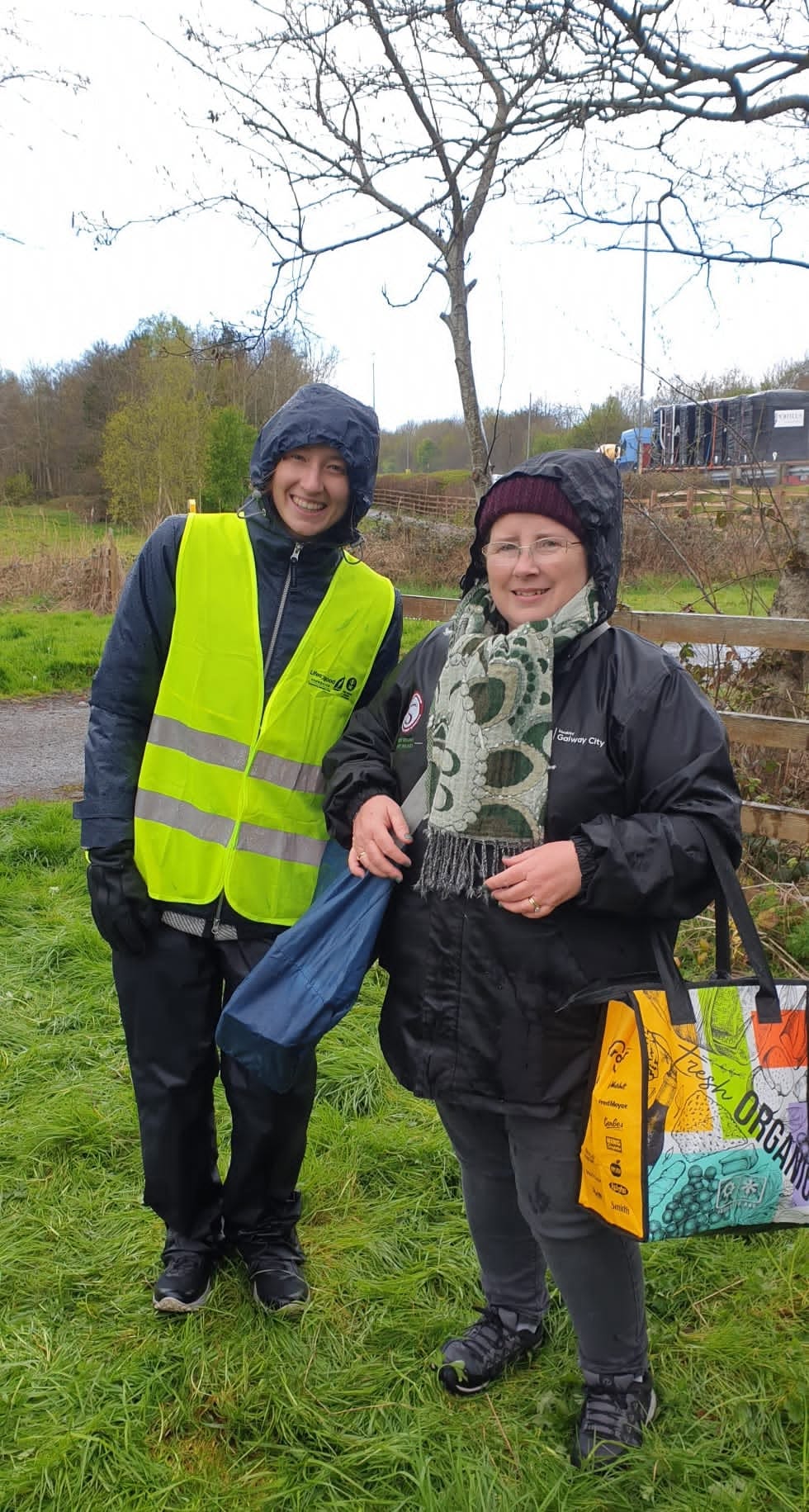 Two people in rain jackets at a community clean-up beside a field